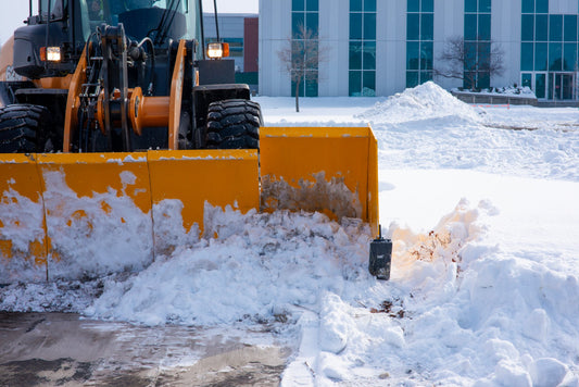 Snow plow clearing snow from a driveway in front of a building