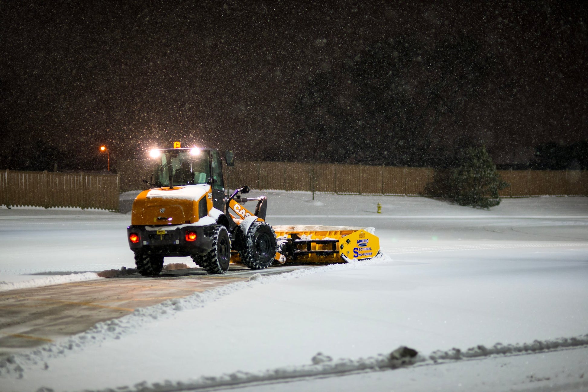 Snow plow clearing a driveway at night with snow falling