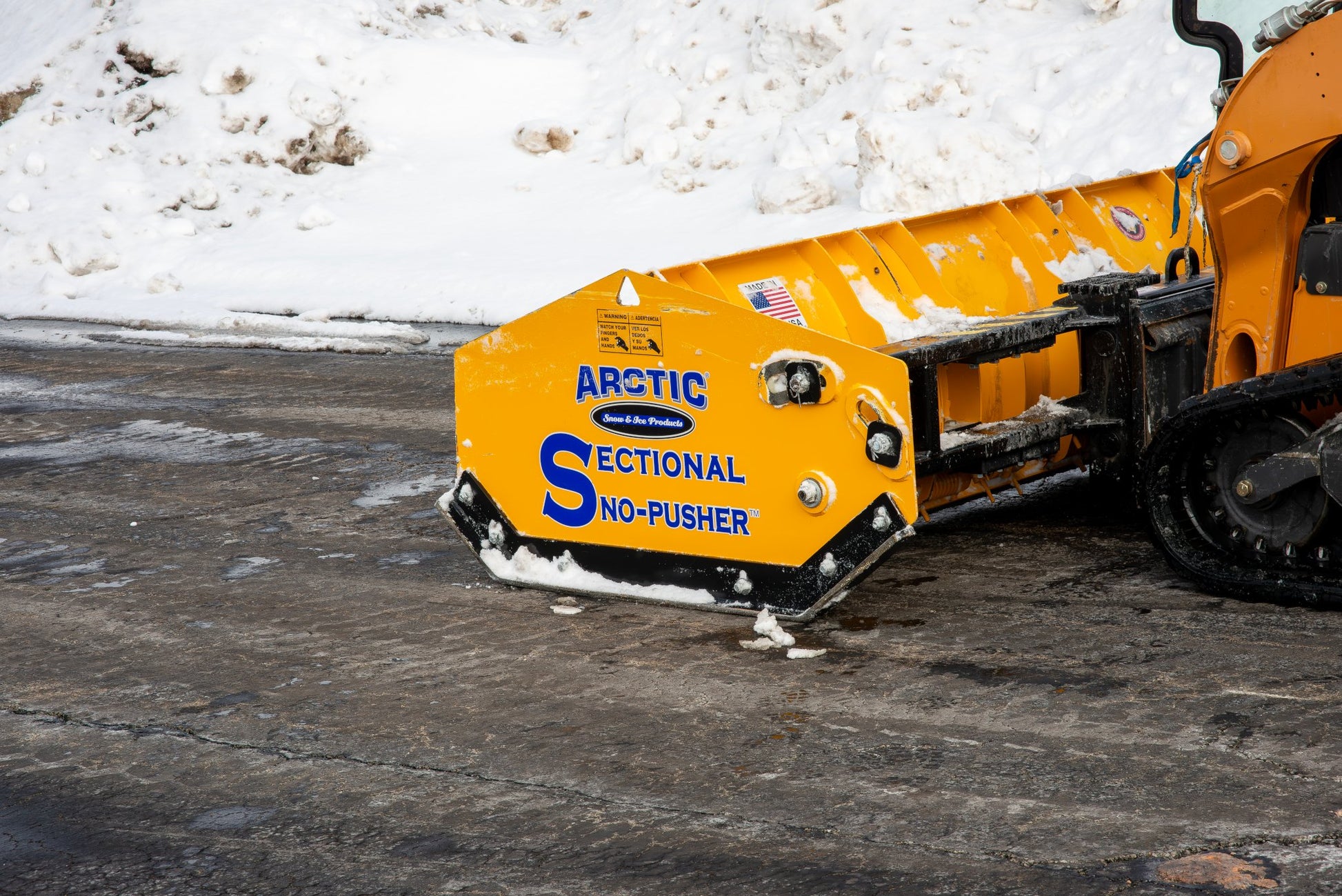 Yellow snow removal machine with 'Arctic Sectional No-Pusher' branding on a snowy background.