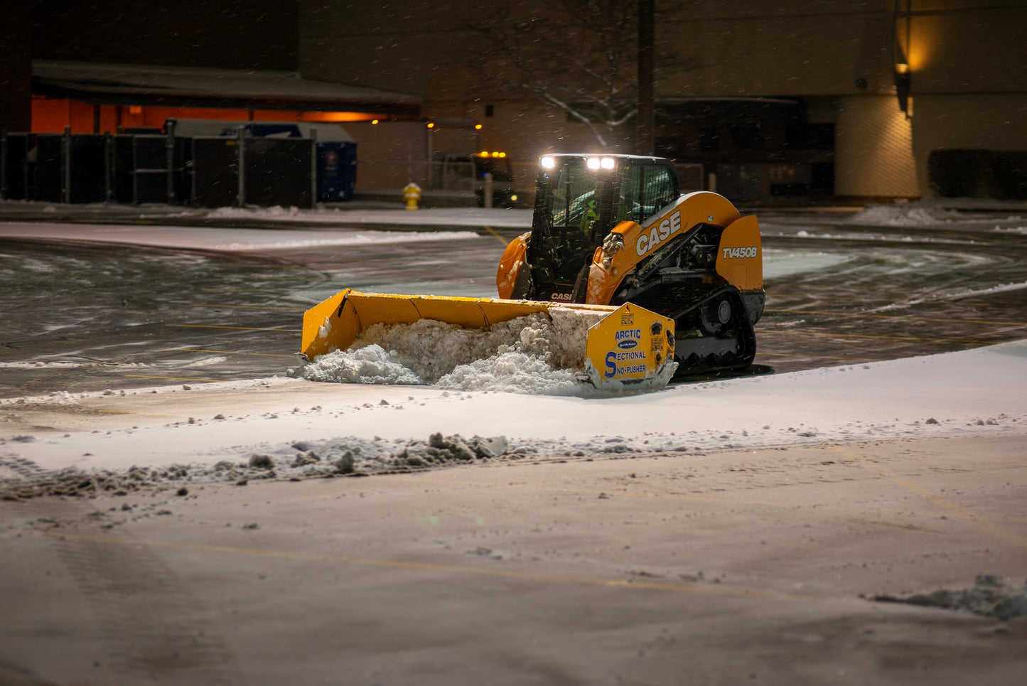 Snow plow clearing snow from a parking lot at night